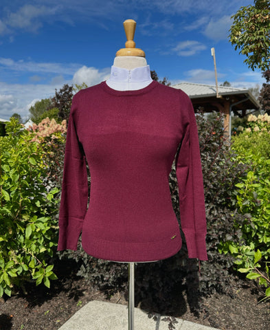 Maroon sweater on a mannequin outdoors with greenery and blue sky in the background