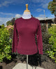 Maroon sweater on a mannequin outdoors with greenery and blue sky in the background